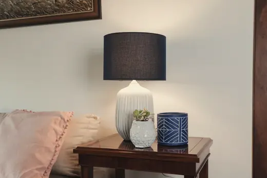 A table lamp with a ribbed white base on a side table, warm evening light